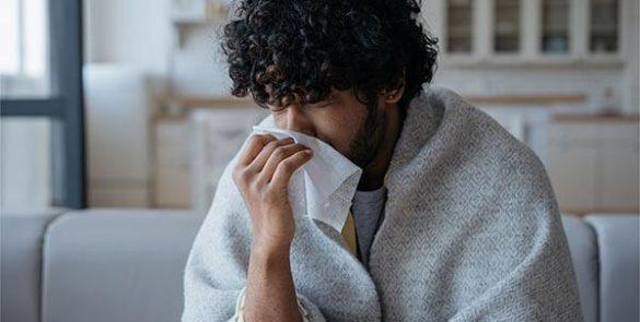 rapaz com gripe a assoar-se no sofá