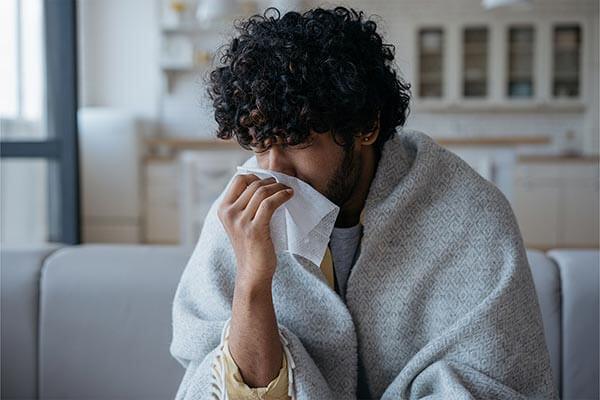 rapaz com gripe a assoar-se no sofá